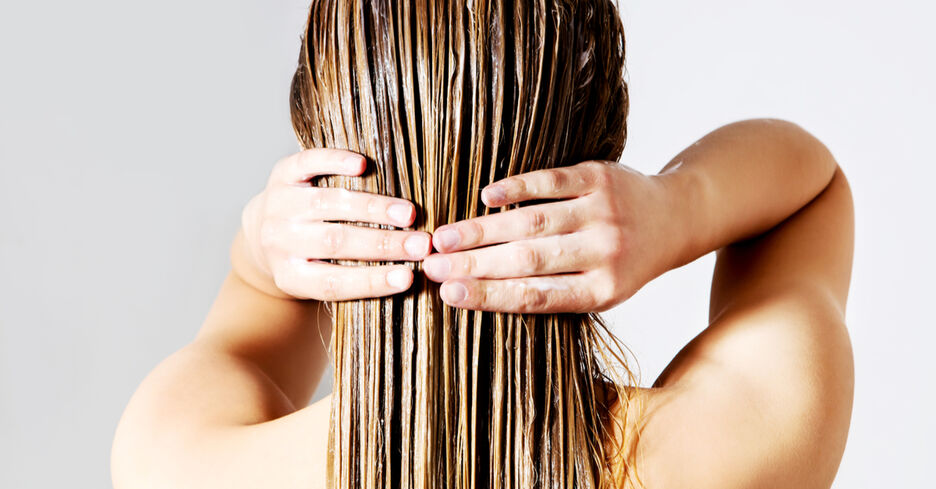 Der Hinterkopf einer Person, die sich mit den Händen ein Haarprodukt in die langen Haare streicht.