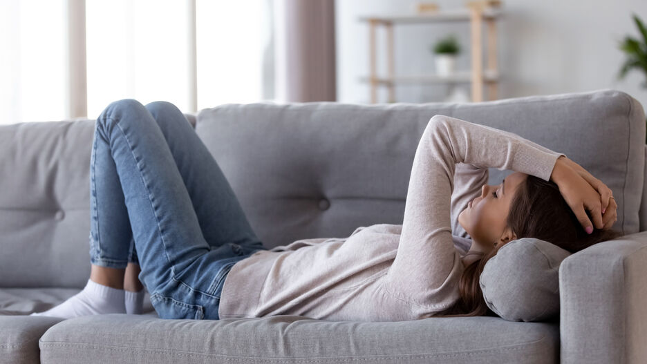 Eine junge Frau liegt erschöpft auf dem Sofa.