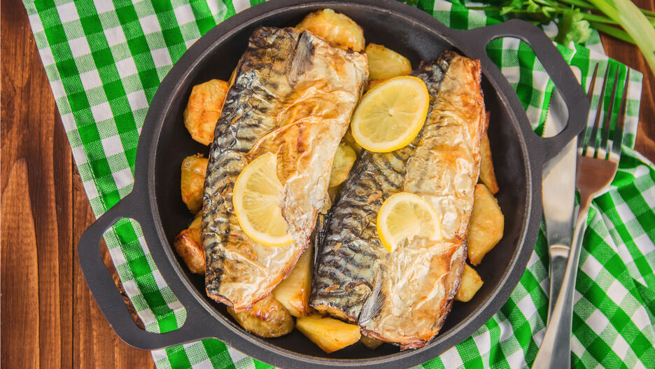 In einer Pfanne liegt zubereiteter Fisch mit Kartoffeln und Zitronenscheiben.