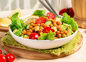 Ein Teller gefüllt mit Salat - Gurke, Avocado, Tomate, Kiechererbsen.