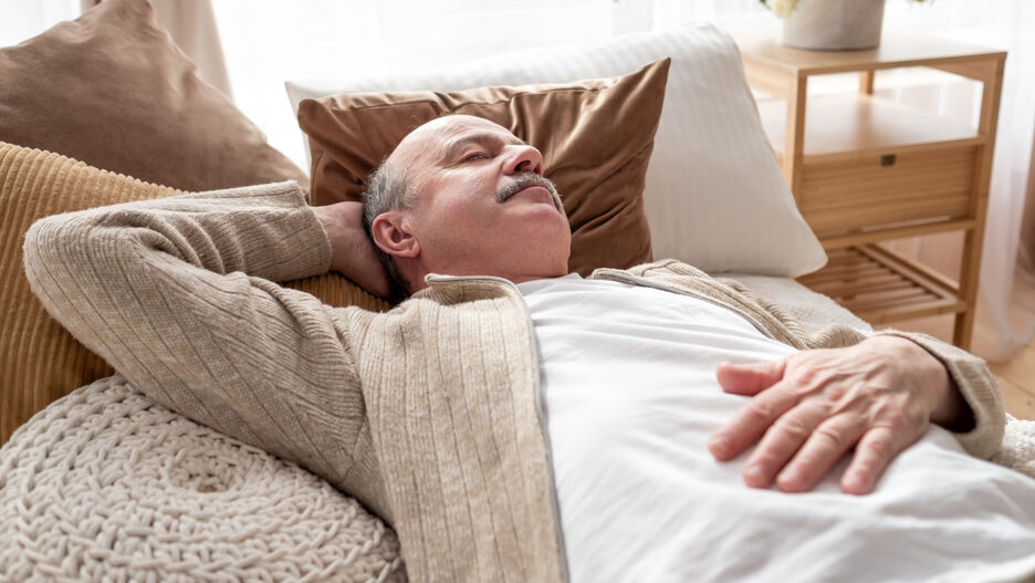 Ein älterer Mann liegt auf der Couch und schläft.