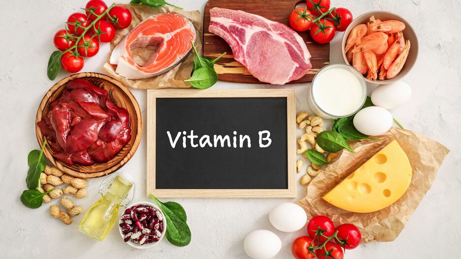 Auf einem Tisch liegen unterschiedliche Lebensmittel, die Vitamin B enthalten. In der Mitte befindet sich ein Schild, auf dem "Vitamin B" steht.