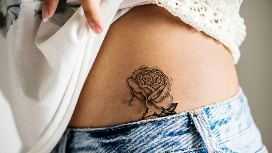 Ein Rosen-Tattoo ziert die Taille einer Frau.