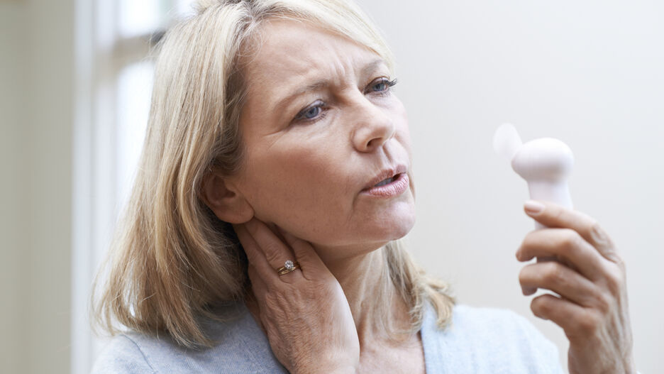 Abgebildet ist eine blonde Dame, die sich einen Handventilator vor das Gesicht hält.