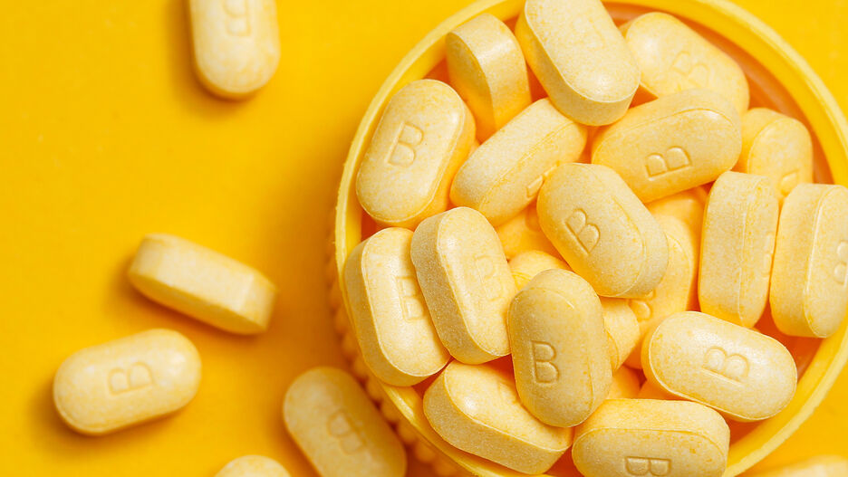 Mehrere Vitamin-B-Tabletten liegen auf einem gelben Untergrund.