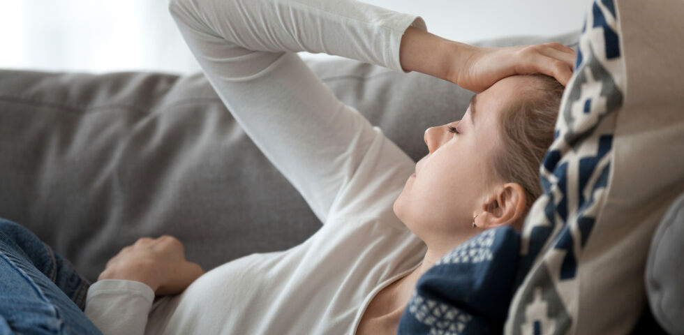 Frau liegt auf Sofa und hält sich Kopf. Sie hat Schwindel oder Kopfschmerzen. - Alle Arten von Schwindel (Vertigo) sind für die Betroffenen extrem belastend. - © Shutterstock