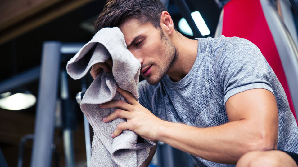 Fitnessstudio Sport_Mann trocknet sich mit einem Handtuch ab